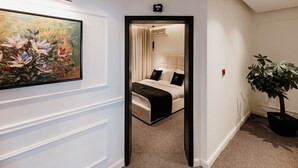 A hotel hallway with a bed, a painting, and a potted plant.