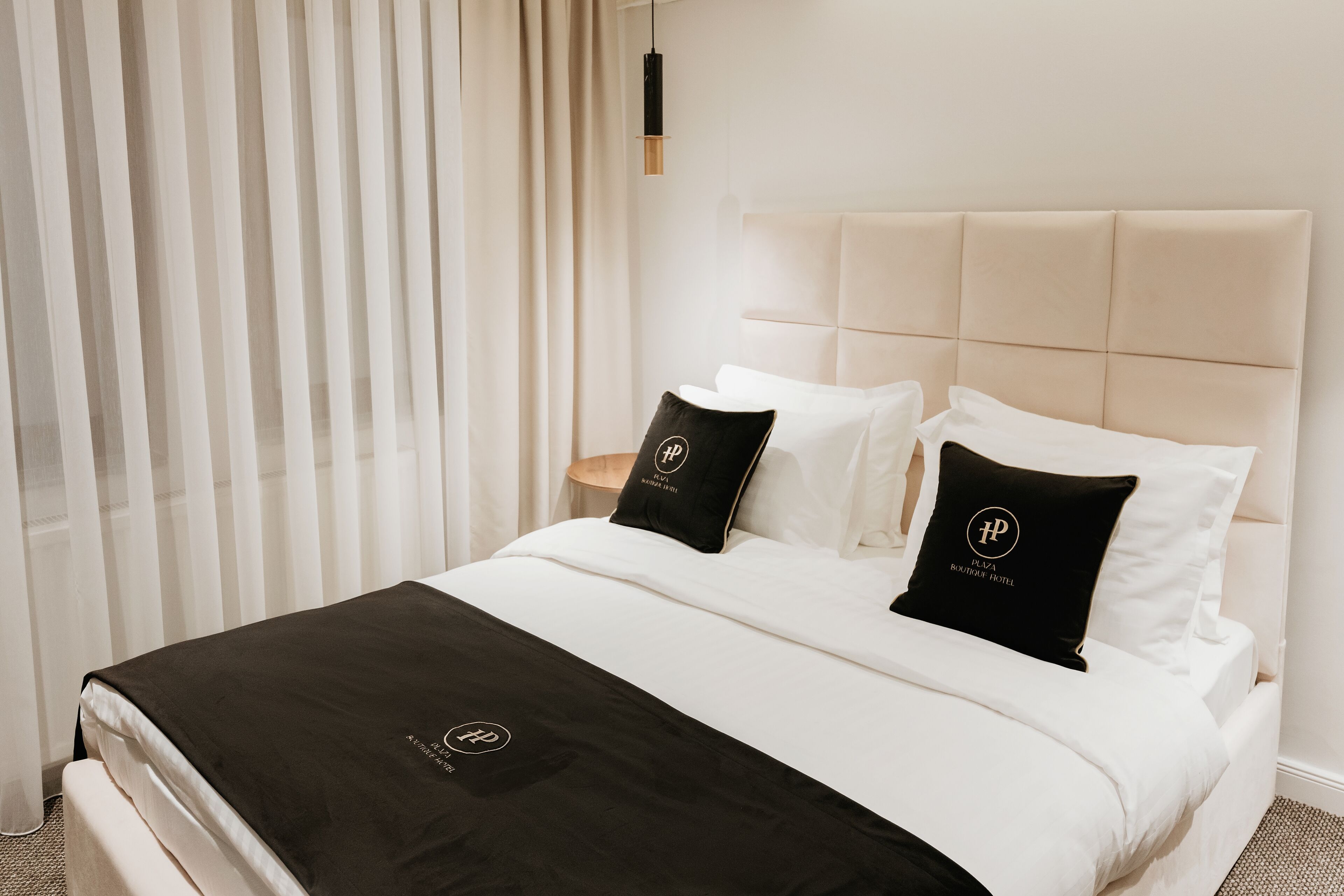 A hotel room with a bed, white bedding, a black throw, and two black pillows with a logo.