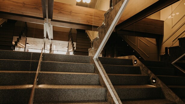 A staircase with a wooden handrail and carpeted steps, leading to an upper level.