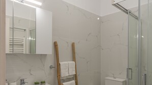 Un baño moderno con cabina de ducha de vidrio, un lavabo blanco con espejo y un inodoro con protector de salpicadura de mármol.