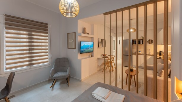 Un dormitorio moderno con una cama, una silla, un televisor y una puerta corredera que da a una cocina.