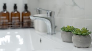 Un baño con un lavamanos blanco, un grifo moderno y tres botellas de líquido anaranjado en la encimera.