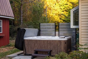 A hot tub in a backyard with a wooden deck, a red shed, and a house with a window.