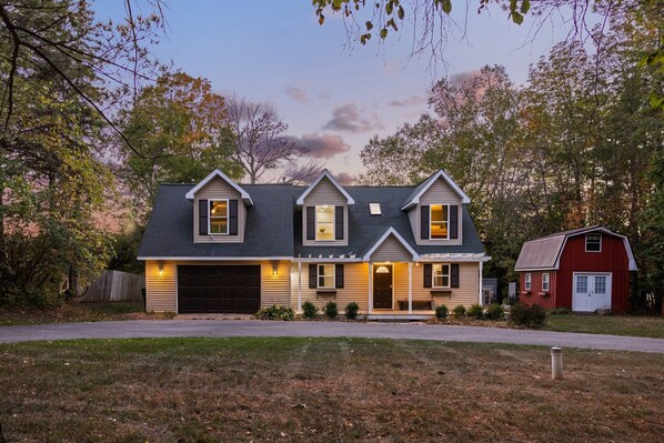 A two-story house with a garage, a front porch, and a red barn in the background.