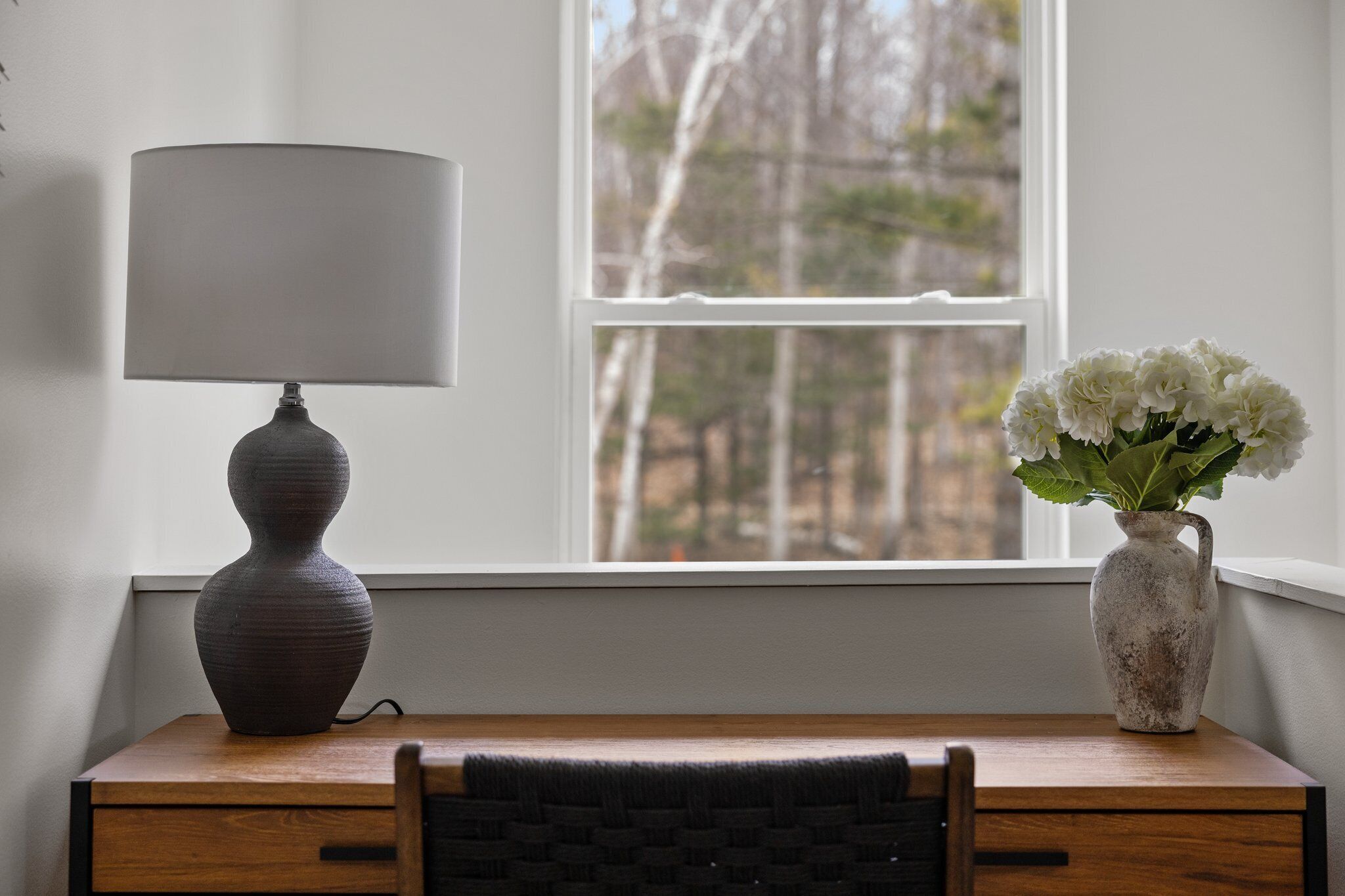 A desk with a lamp and a vase of flowers by a window.
