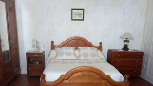 Un llit de fusta amb capçal, dues taules de nit, un mirall i una làmpada.