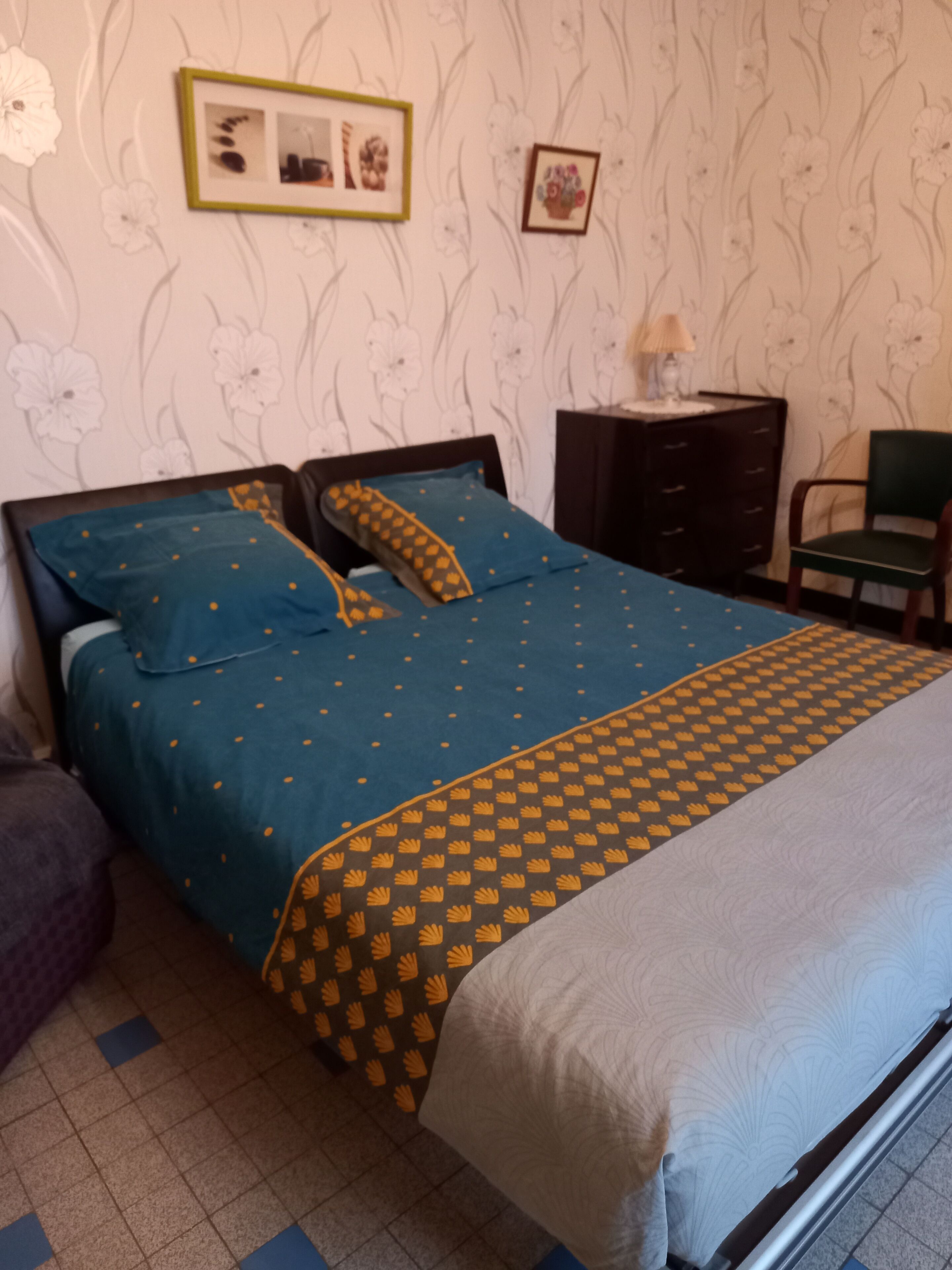 Ein Schlafzimmer mit einem Bett, einer Kommode, einem Sessel und einer Wand mit floralem Wandpapier.