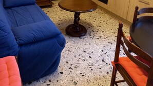 Un espai habitable compacte amb un sofà, una taula de dinar i una cuina que inclou armaris i electrodomèstics.