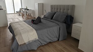 Un dormitorio moderno con una cama gris, una mesita de noche, un armario y un escritorio con una silla.