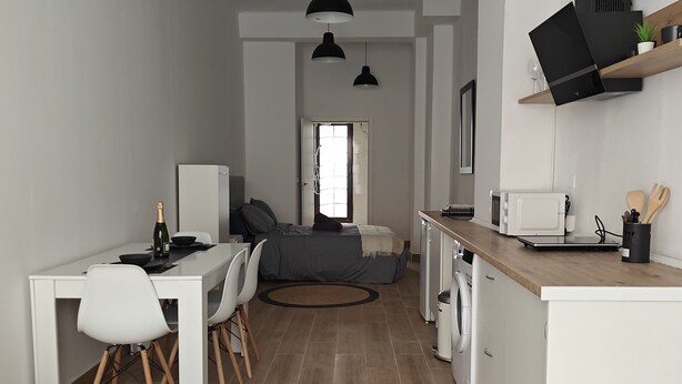Una cocina moderna con armarios blancos, encimera de madera y lámparas colgantes negras.