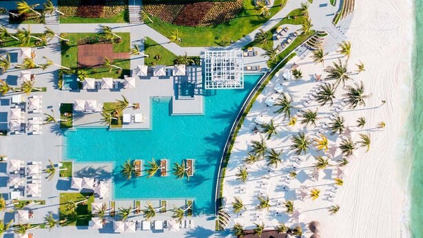 Vista aérea de un resort con una piscina grande, tumbonas y una zona de playa.