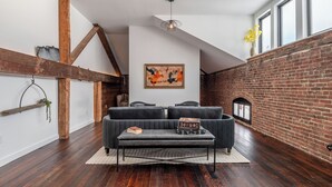 A modern living room with a dark grey sofa, a black coffee table, and a rustic brick wall. - Abacus Suite at Spofford Lodge (Bucksport)