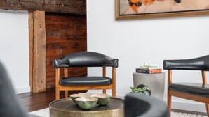 A modern living room with a wooden accent wall, two leather chairs, a coffee table with decorative bowls, and a framed abstract painting. - Abacus Suite at Spofford Lodge (Bucksport)