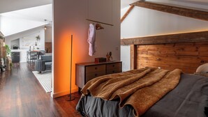 A modern bedroom with a large bed, wooden headboard, and a view of a kitchen and living area. - Abacus Suite at Spofford Lodge (Bucksport)