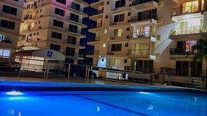 Un hotel de varios pisos con balcones, una piscina y estacionamiento techado.