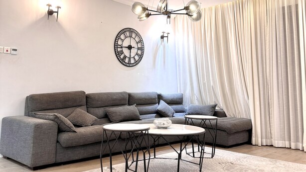 Una sala de estar moderna con un sofá seccional gris, una mesa de centro redonda y una araña.