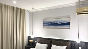 Una habitación de hotel moderna con una cama grande, un cabecero oscuro, una mesita de noche con una lámpara y un aire acondicionado instalado en la pared.