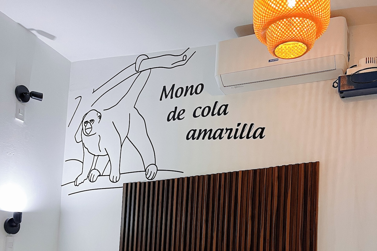 Habitación de hotel con dos camas, cabecero de madera, aire acondicionado de pared, lámpara colgante y un adorno de pared con un mono.