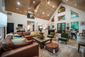 A spacious living area with a high ceiling, wooden beams, and large windows.