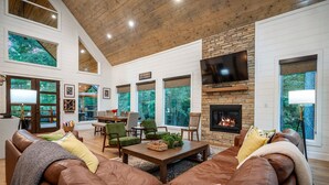 A spacious living room with a fireplace, leather sofas, and large windows offering a view of the outdoors.