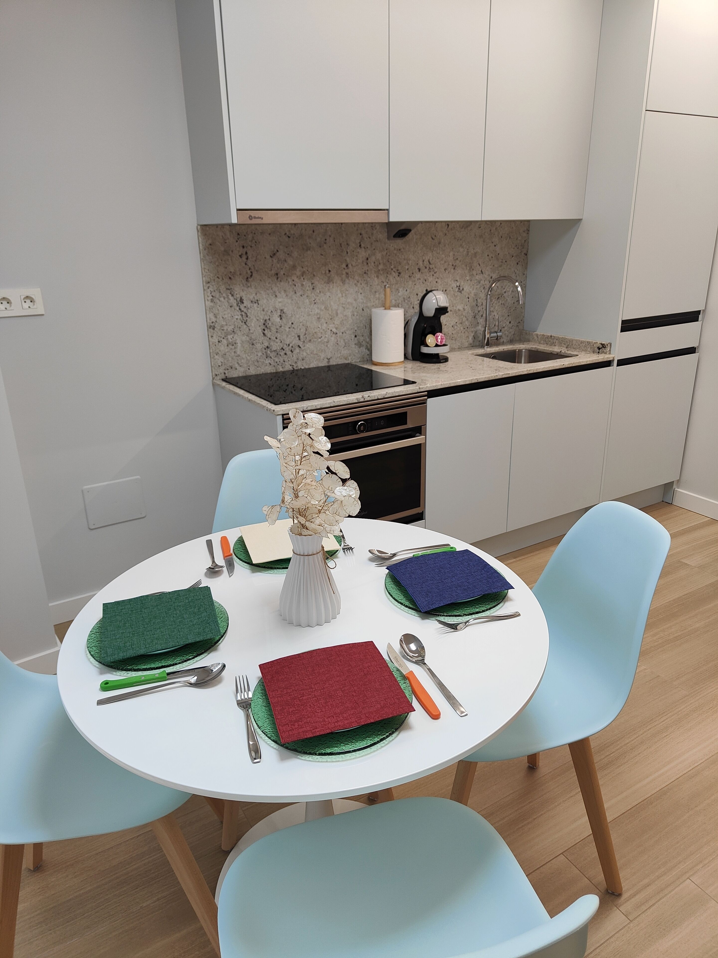 Una cocina moderna con armarios blancos, encimera de granito y comedor con una mesa redonda para cuatro.