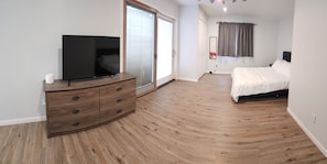 Relax in a serene bedroom with a large bed, flat-screen TV, and a window with curtains.