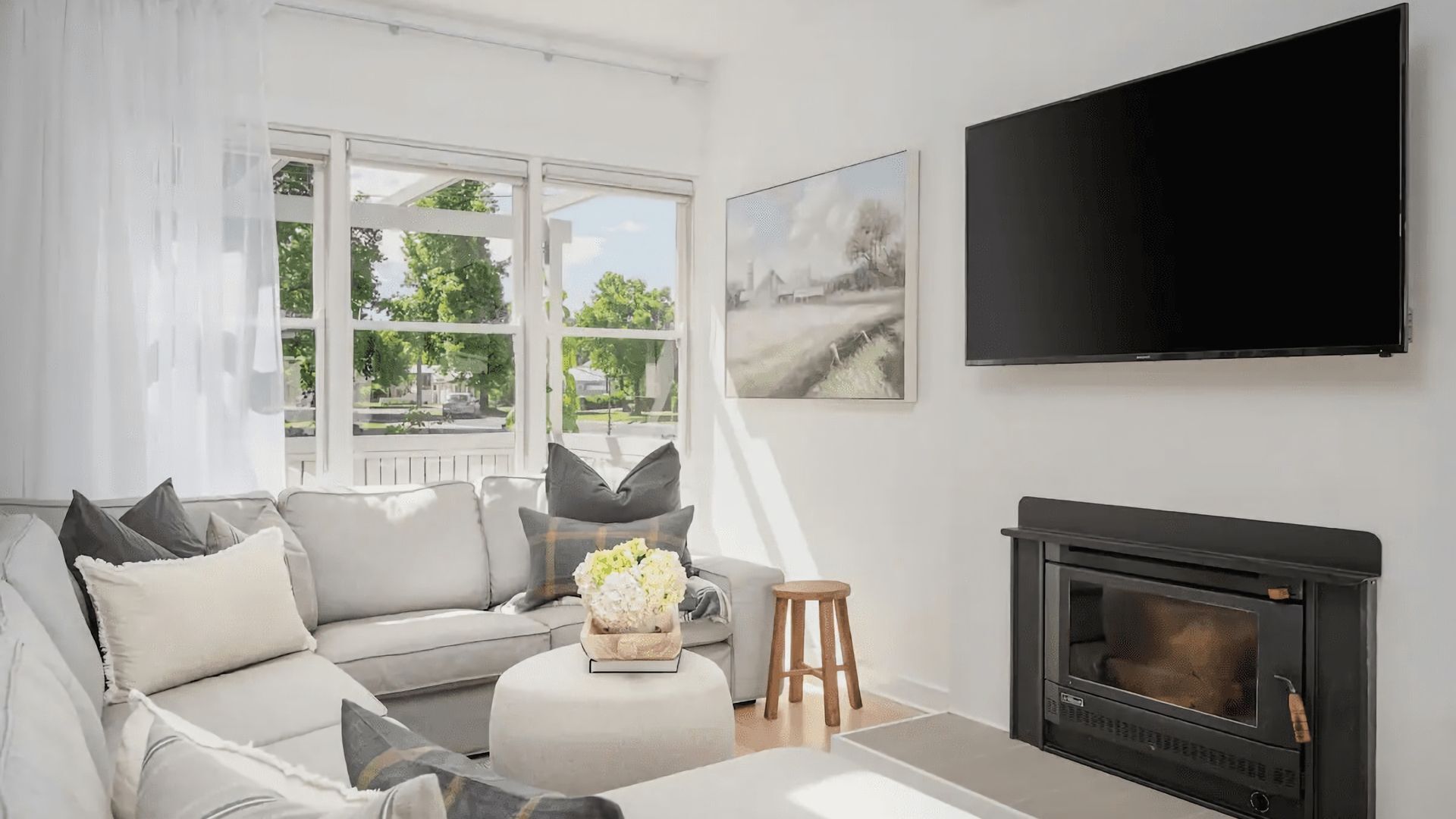 Una sala de estar moderna con un sofá, una mesa de centro con flores, una chimenea y un televisor grande en la pared.