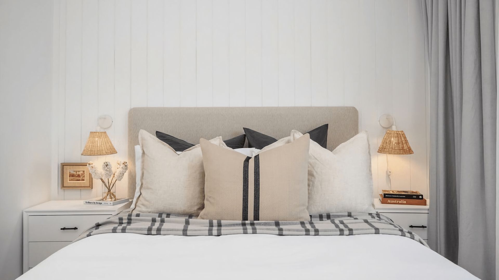 A neatly made bed with a plaid bedspread, a headboard, and multiple pillows. There are two bedside tables with lamps and a framed picture on one.