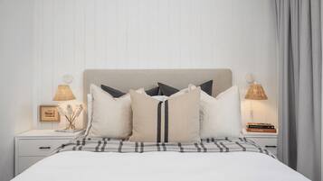 A neatly made bed with a plaid bedspread, a headboard, and multiple pillows. There are two bedside tables with lamps and a framed picture on one.