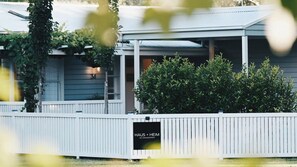 A building with a white fence, a sign reading 'HAUS + HEIM ACCOMMODATION', and a covered porch area.