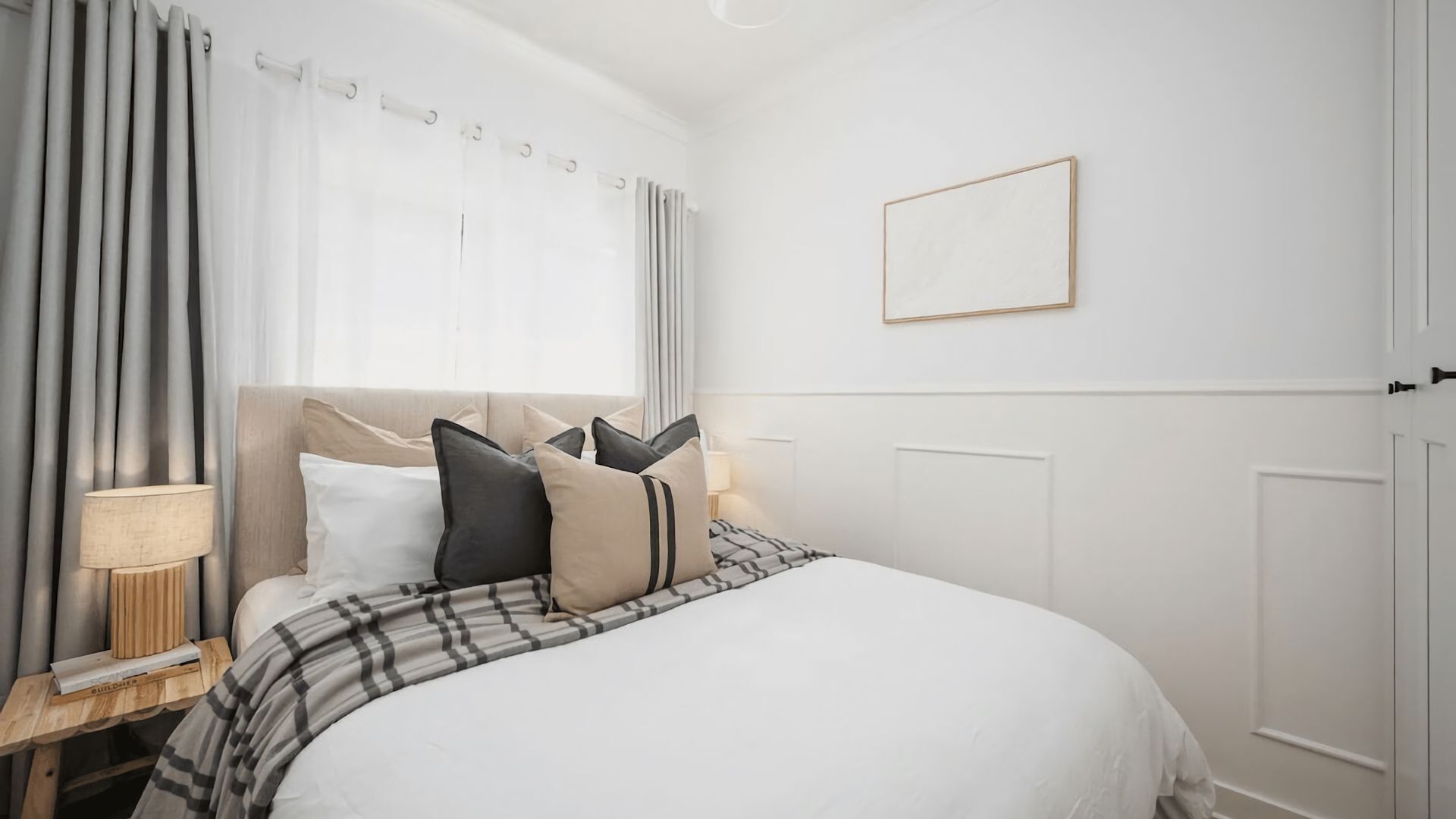 A hotel room with a bed, curtains, a bedside table with a lamp, and a framed picture on the wall.