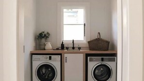 A laundry room with two washing machines, a sink, a window, and a basket on the countertop.