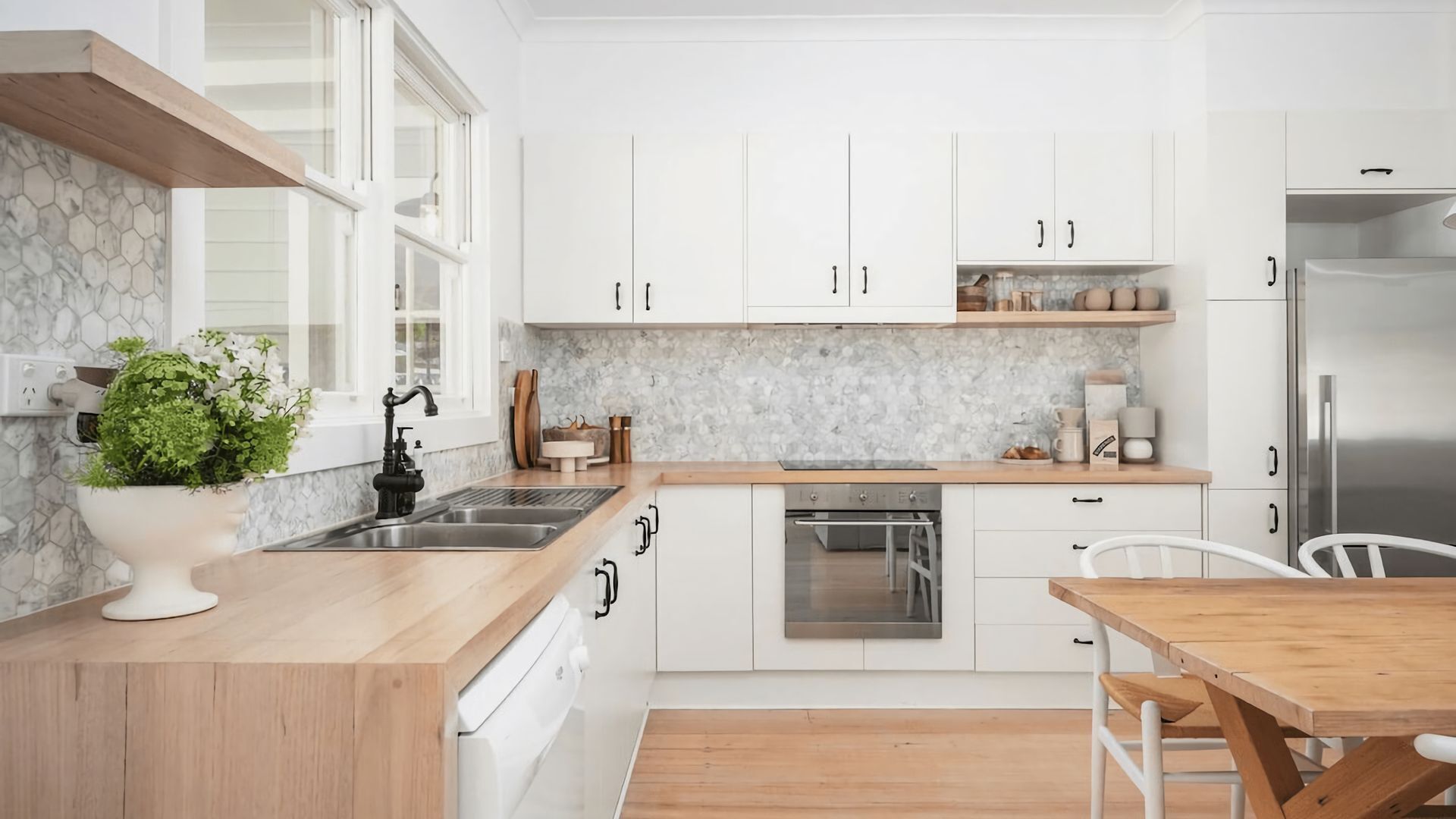 A modern kitchen with white cabinets, a stainless steel sink, and a wooden countertop.