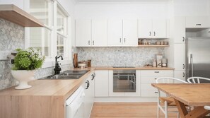 A modern kitchen with white cabinets, a stainless steel sink, and a wooden countertop.