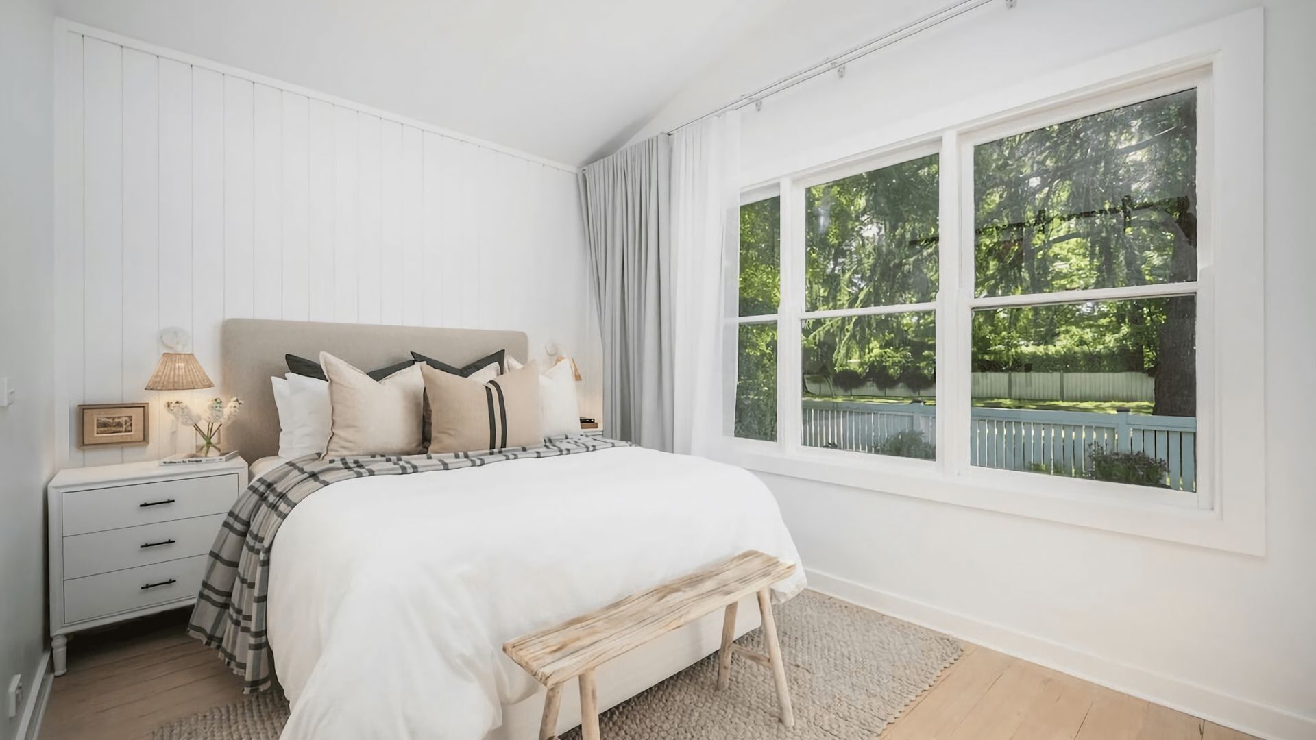 Un dormitorio con cama, mesita de noche, lámpara y ventana con vista a zonas verdes.