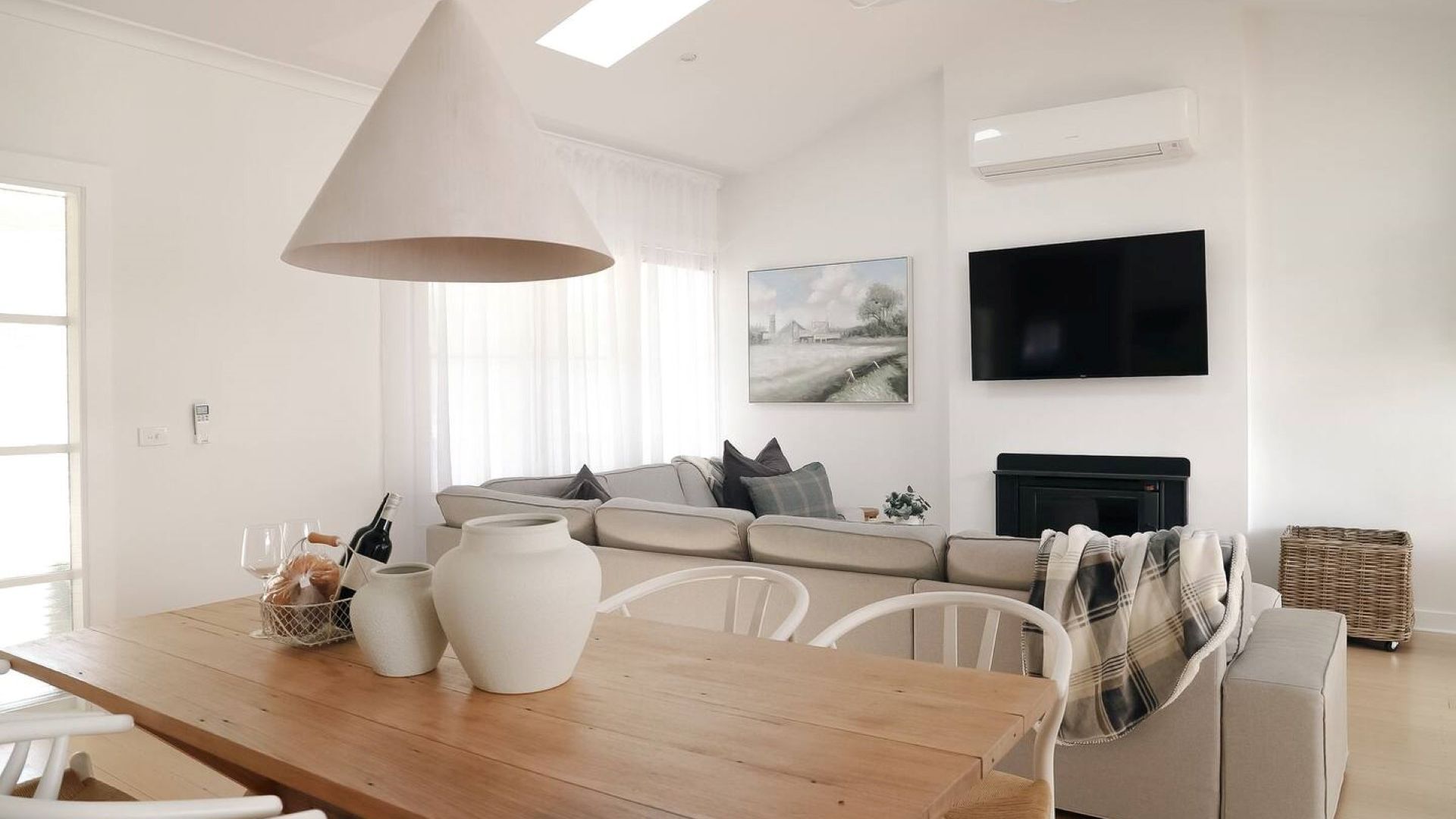 Een moderne woonkamer met een houten eettafel, witte stoelen, een bank, een open haard en een flatscreen televisie aan de muur.