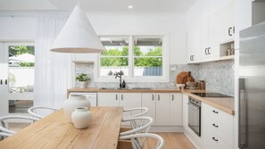 A modern kitchen with white cabinetry, a wooden dining table, and a large window with a view of greenery.