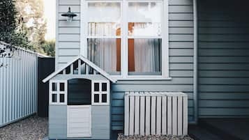 Een huis met een klein speelhuisje, een raam met gordijnen en een witte hek.