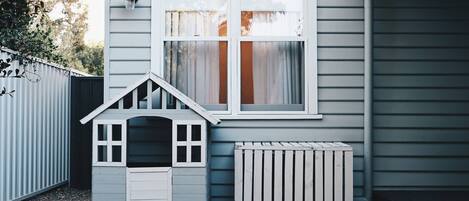 Una casa con una casita de juegos, una ventana con cortinas y una cerca blanca.