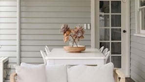 Une table à manger blanche, agrémentée d’un centre de table en forme de saladier en bois, des chaises blanches à revêtement clair et une porte blanche en arrière-plan.