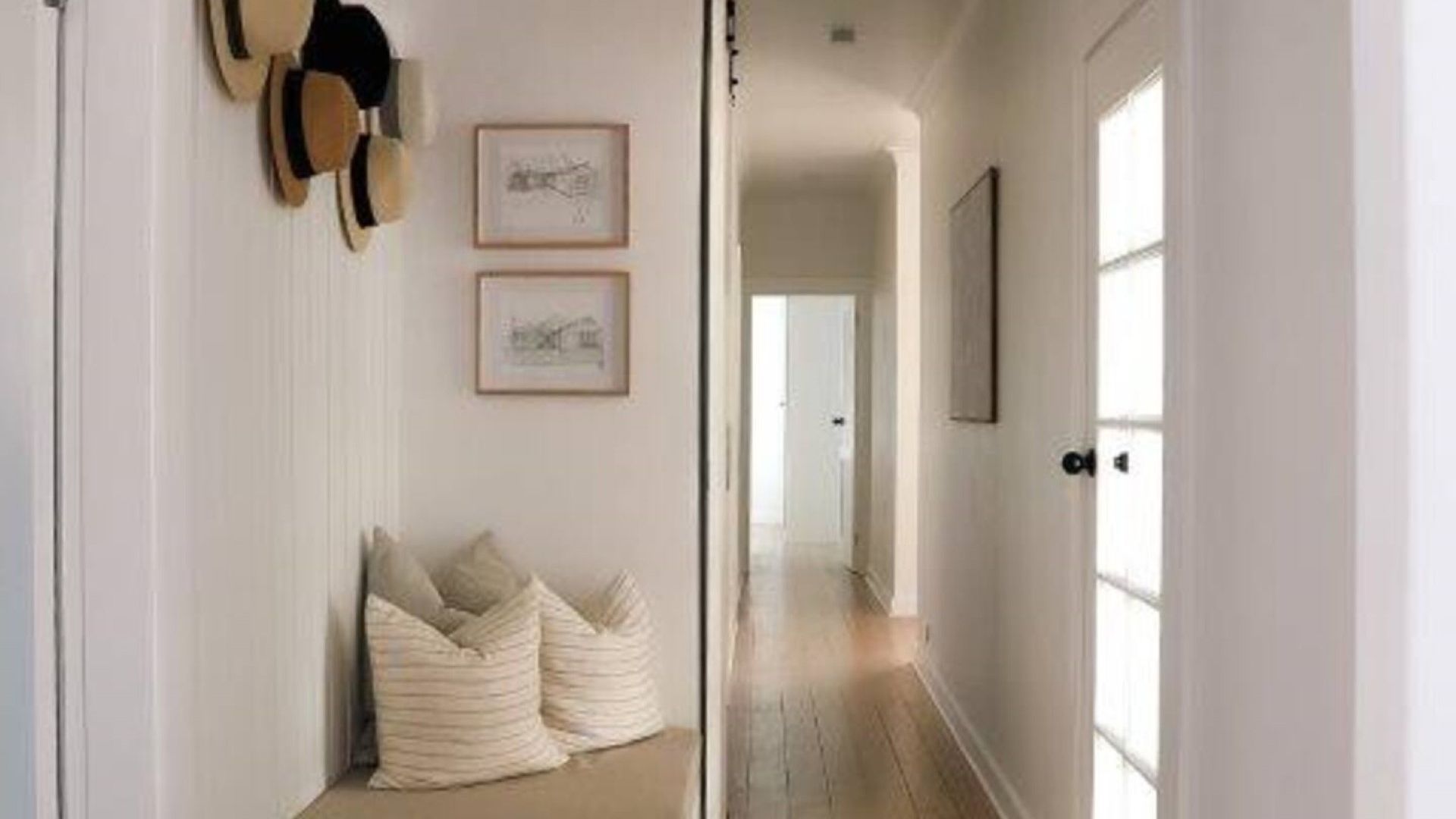 A hallway with a door leading to another room, a framed picture on the wall, and a pair of cushions on the floor.