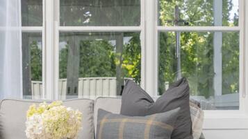 A room with a large window, a sofa with cushions, and a vase of flowers.