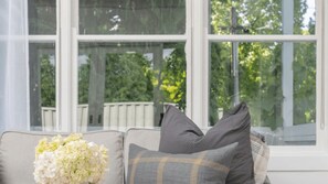 A room with a large window, a sofa with cushions, and a vase of flowers.