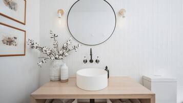 A bathroom with a round mirror, white tiles, a wooden vanity, and two framed artworks.
