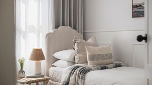 A bedroom with a bed, pillows, a bedside table with a lamp, a book, and a vase with flowers.