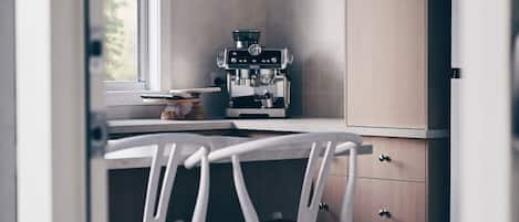 Una cocina con cafetera, una ventana y una silla blanca.