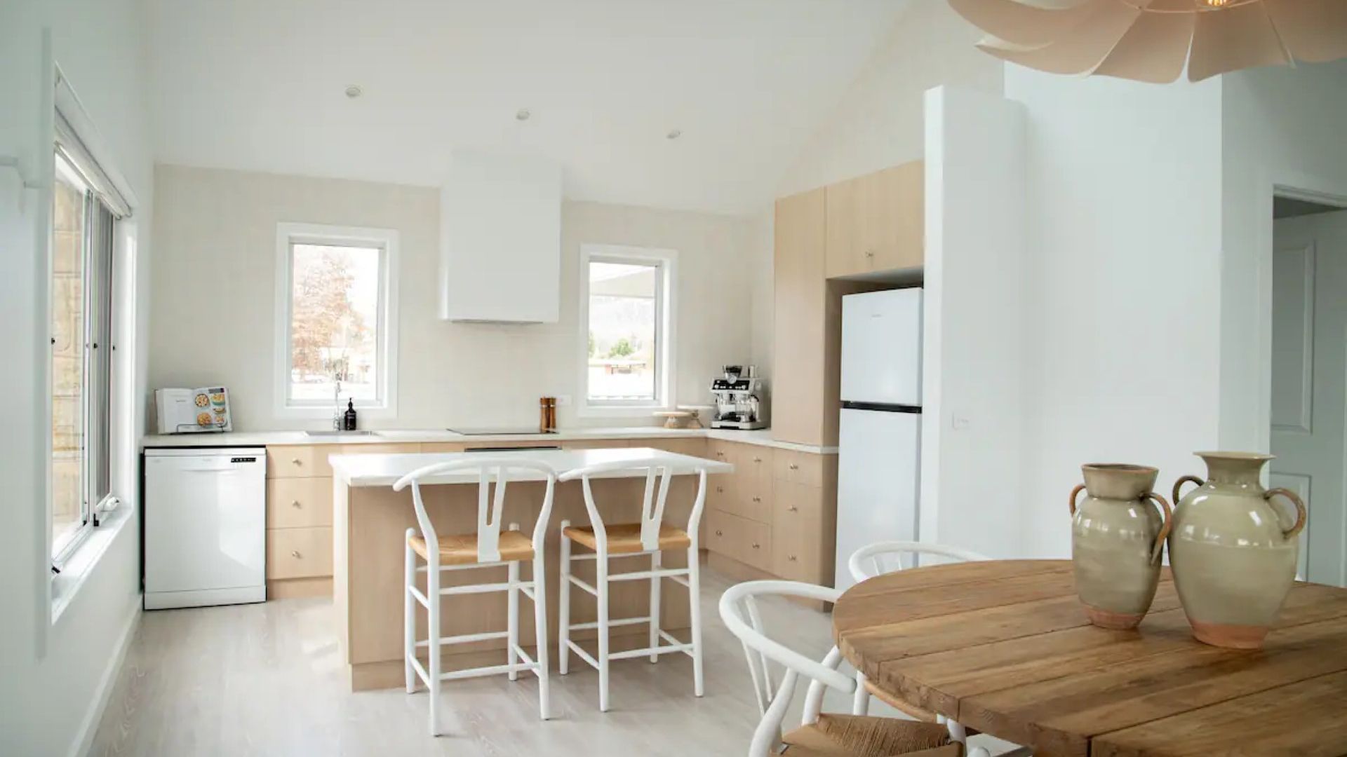 Une cuisine moderne avec des meubles blancs, un îlot central doté de chaises, un réfrigérateur et une machine à café.