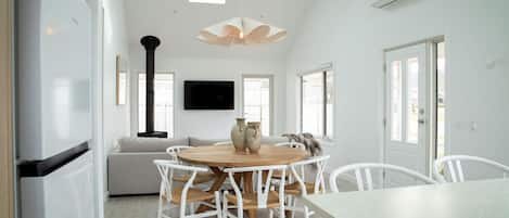 A modern kitchen with white cabinetry, a central island with seating, a flat-screen TV, and a large window providing natural light.