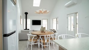 A modern kitchen with white cabinetry, a central island with seating, a flat-screen TV, and a large window providing natural light.