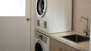 Un espace buanderie compact comprenant un lave-linge, un sèche-linge et un évier.